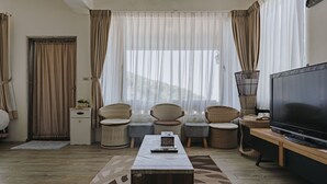 A living room with a large flat-screen TV, wicker furniture, a coffee table, and a view through sheer curtains. - Mountain Traveler Inn (New Taipei City)