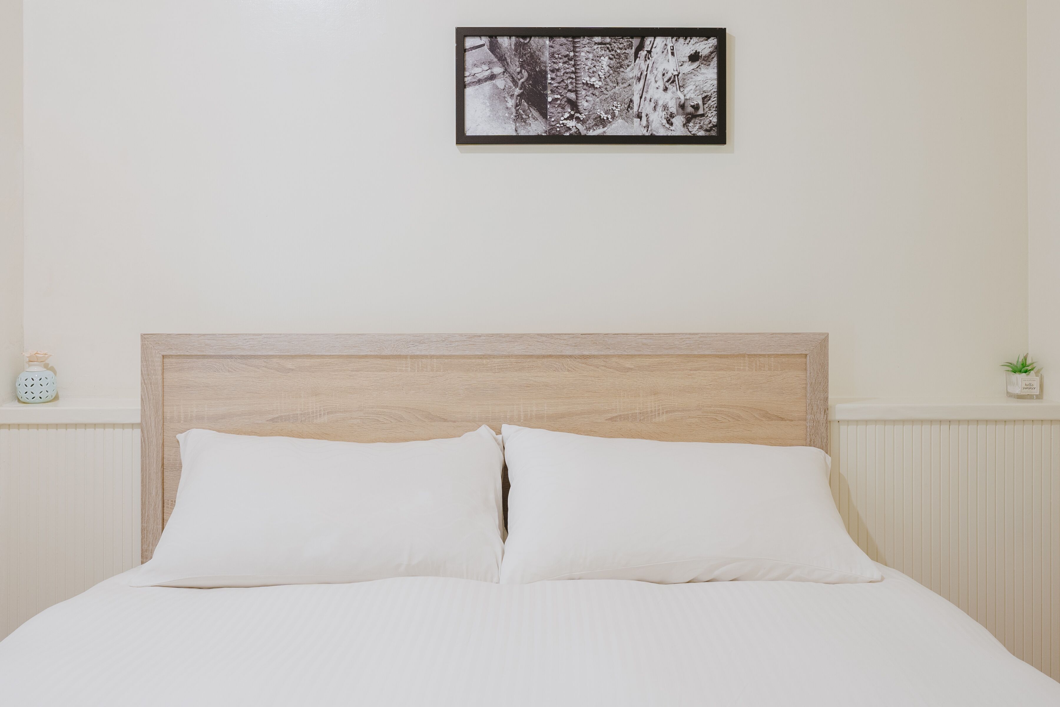 Un lit bien fait, avec une tête de lit en bois, une petite table de chevet avec une lampe et un tableau encadré accroché au mur.