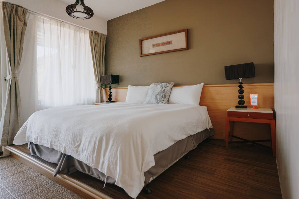 A neatly made bed with a wooden headboard, a bedside table with a lamp, and a framed picture on the wall.
