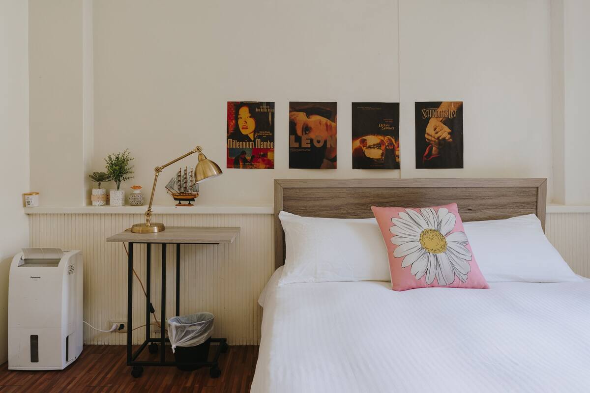 A bedroom with a bed, a nightstand, a lamp, a radiator, and wall art.