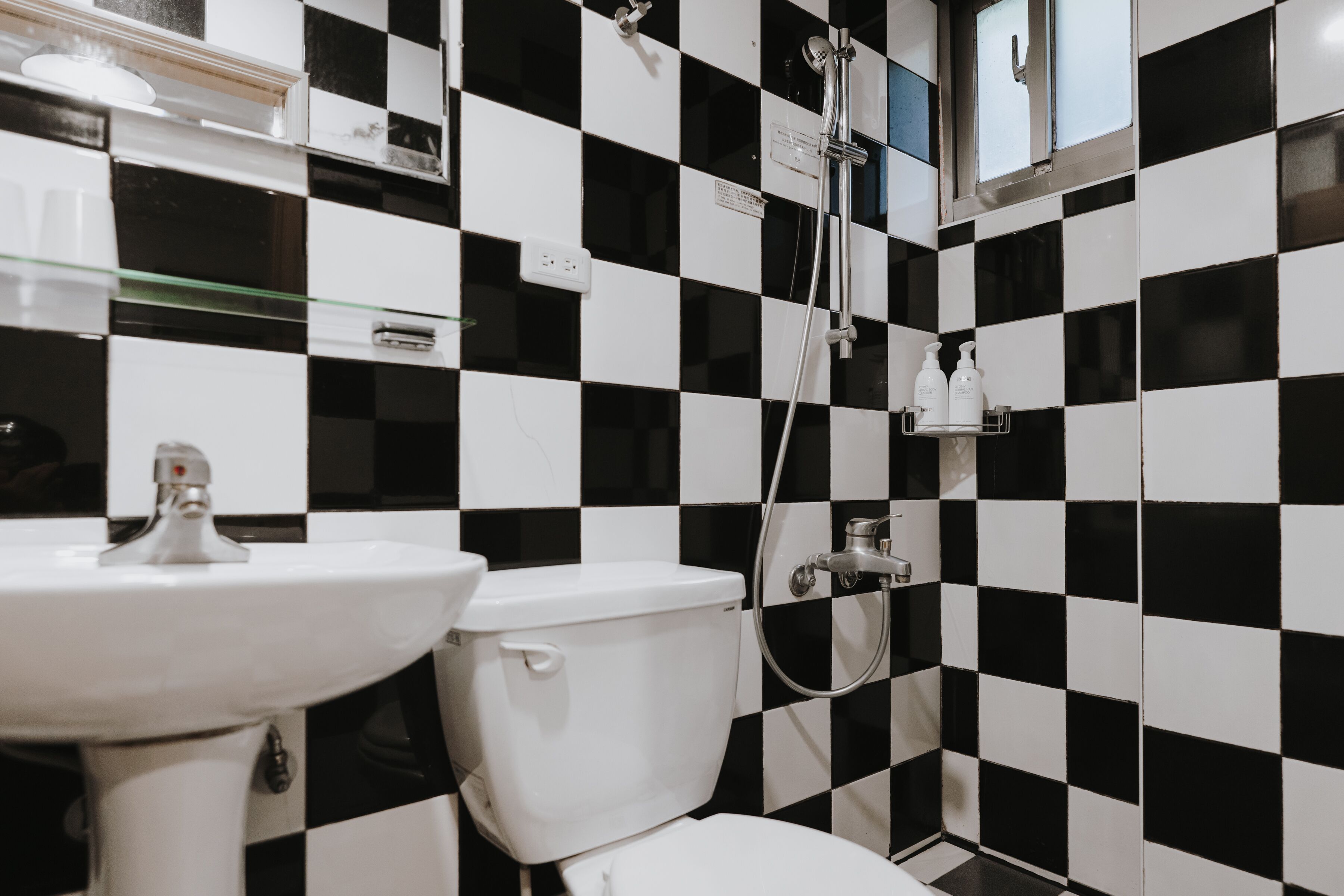 A bathroom with a black and white checkered tile wall, a white sink, and a toilet.
