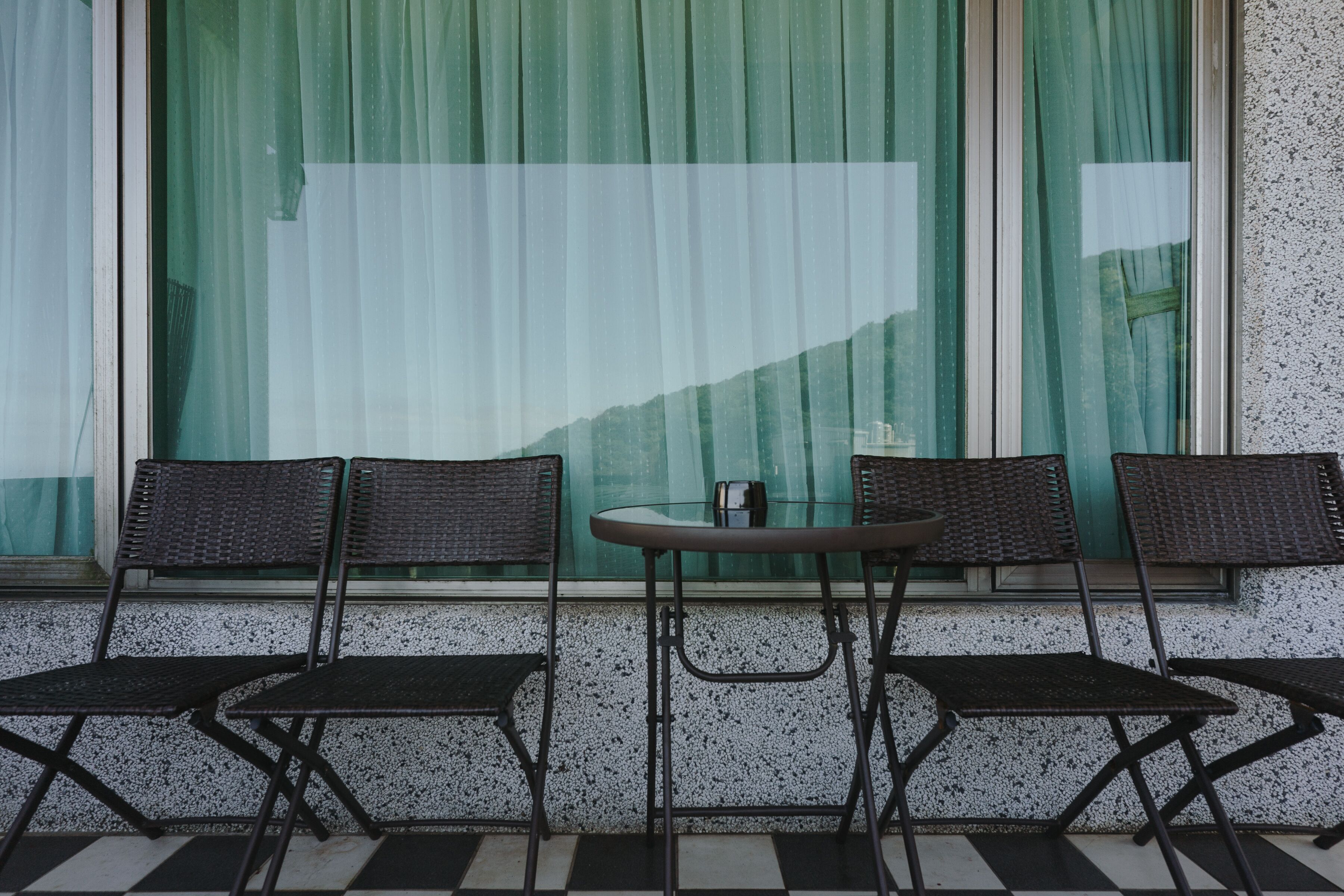 A seating area with three wicker chairs and a small round table, positioned in front of a window with green curtains.