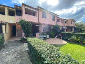 A residential building with a patio area, stone pathway, and greenery.