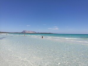 A beach with clear water, people swimming, and a mountain in the background. - Vacation Home 'Villetta Agli Ulivi' near La Cinta Beach with Garden & A/C (San teodoro)