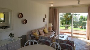 A room with a sofa, a dining table, a chair, a lamp, a mirror, and a view of the outdoors. - Apartment 'Les Fonts 83' with Shared Pool, Private Terrace and Balcony (L'Estartit)