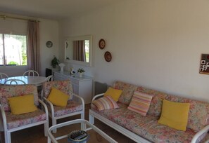 A living room with a sofa, chairs, a table, and a mirror. - Apartment 'Les Fonts 83' with Shared Pool, Private Terrace and Balcony (L'Estartit)