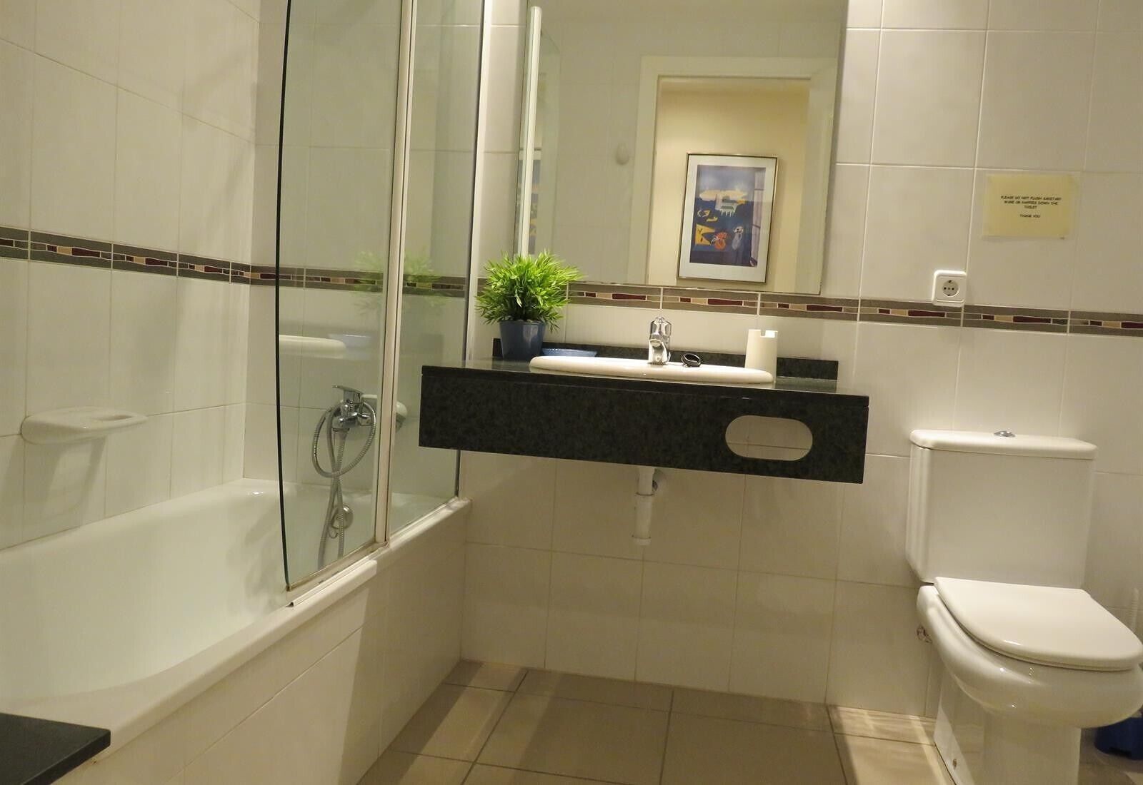 A bathroom with a glass-enclosed shower, a toilet, and a sink with a mirror above it.