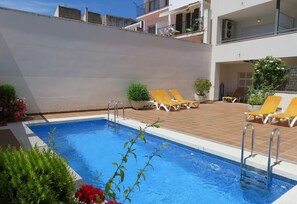 Una piscina con tumbonas y un pequeño jardín.