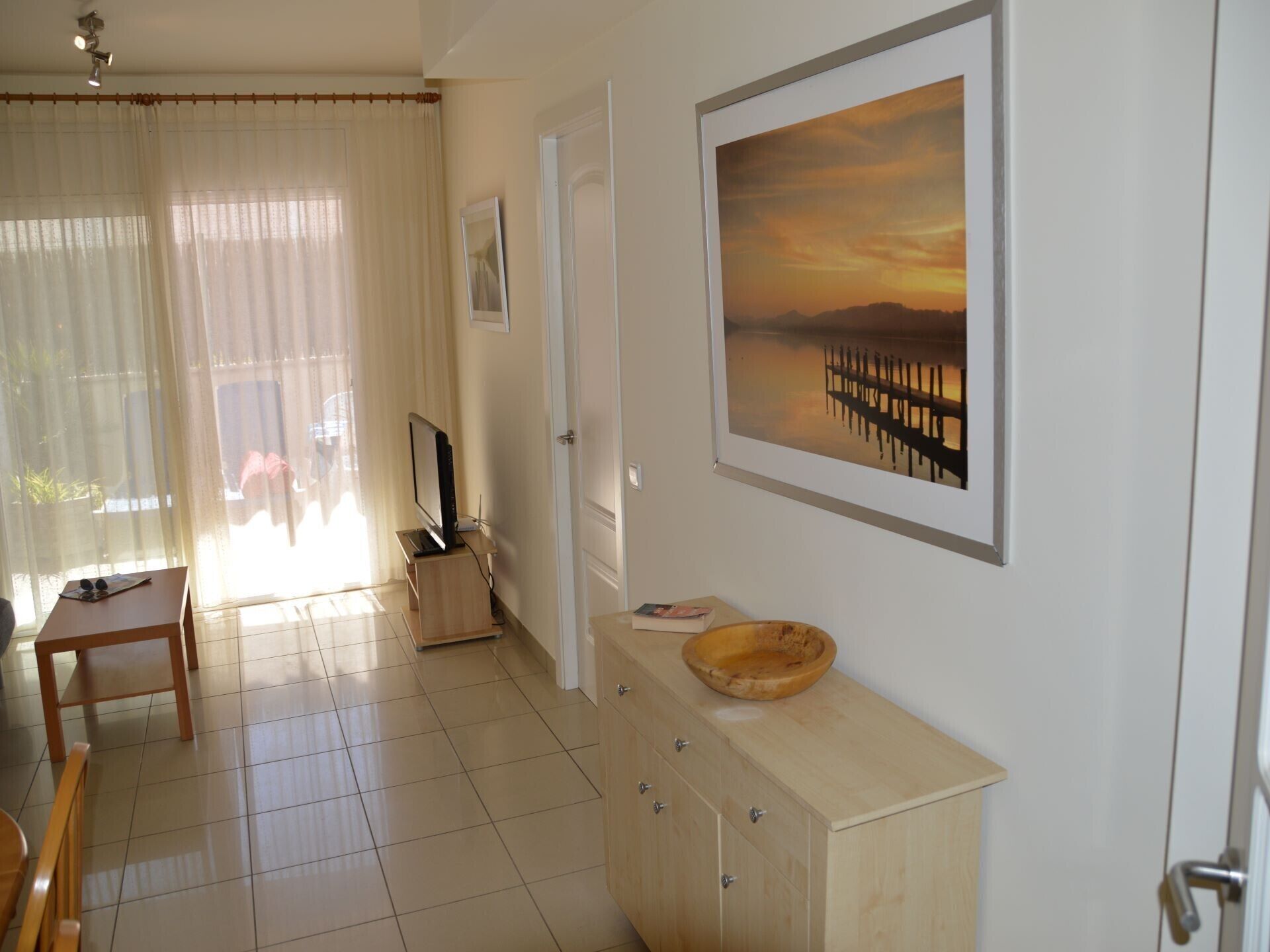 Een kamer met een houten kast, een televisie op een standaard, een lijst met een foto aan de muur en een deur.