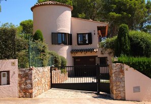 Una casa de dos pisos con fachada de piedra, una torre redonda y un acceso con portones.
