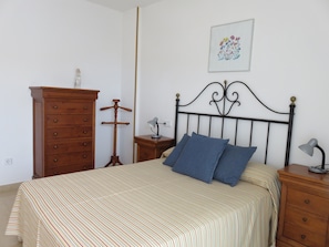 Une chambre à coucher comprenant un lit, une commode, une table de chevet, une lampe et un tableau accroché au mur.
