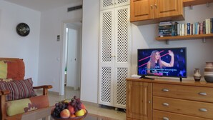 Una sala de estar con televisor, armarios de madera, estantería y frutero.