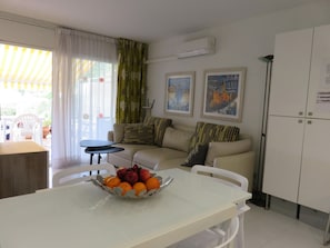 A living room with a sofa, a dining table with fruit, a white cabinet, and artwork on the wall.