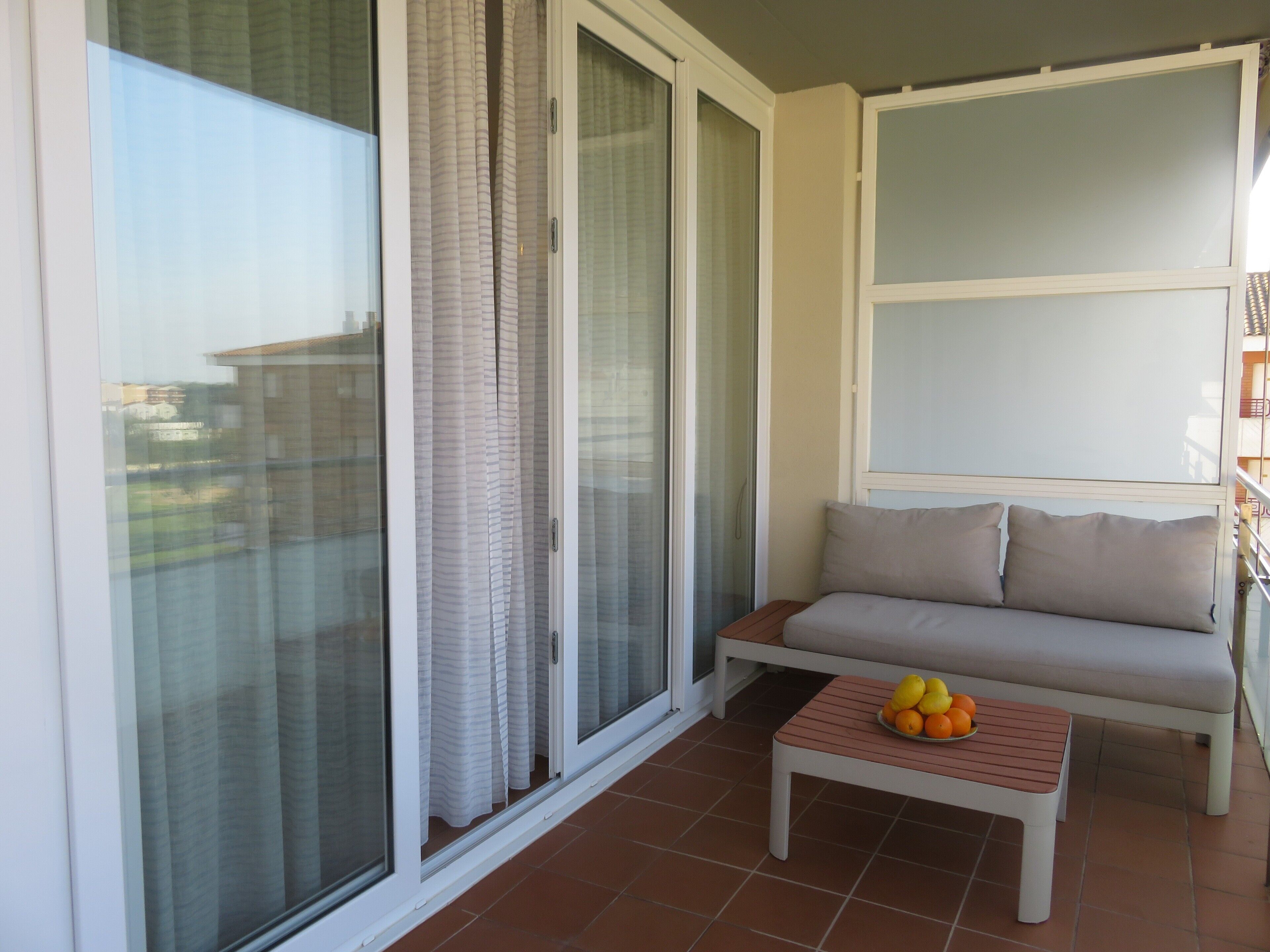 A balcony with a sliding glass door, a white sofa, and a small table with fruit.