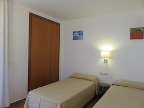 Quarto com duas camas, um guarda-roupa de madeira, uma luminária na parede e duas obras de arte na parede.