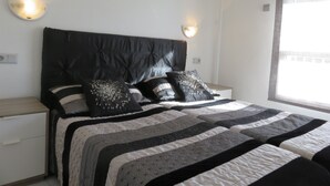 A bedroom with a black headboard, two bedside tables, a bed with a striped bedspread, and two wall-mounted light fixtures.
