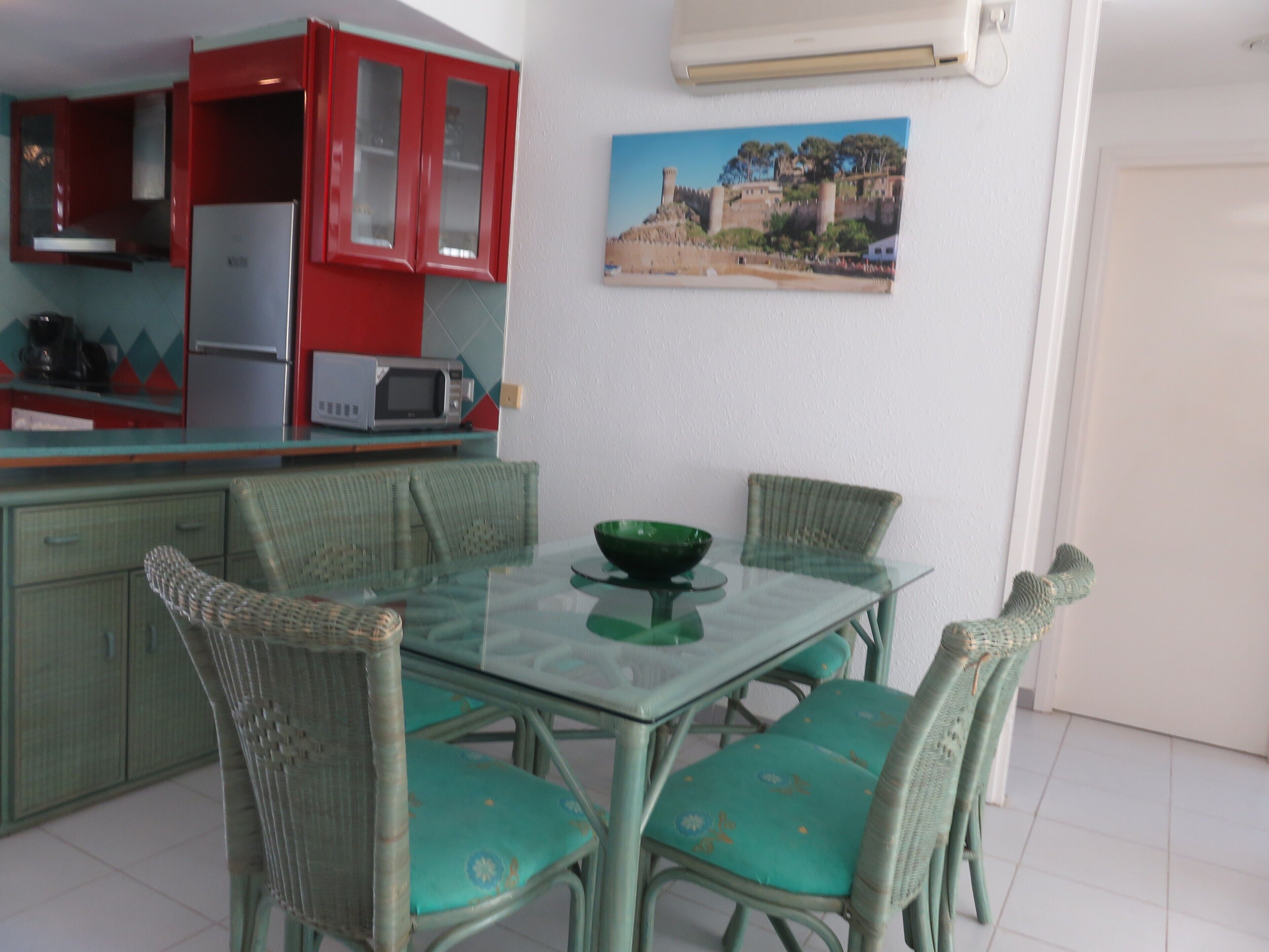 A dining area with a glass table, wicker chairs, and a green bowl.