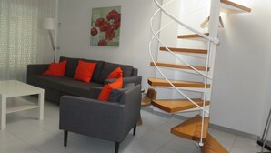 A modern living room with a grey sofa, orange cushions, a white coffee table, and a spiral staircase with wooden steps.