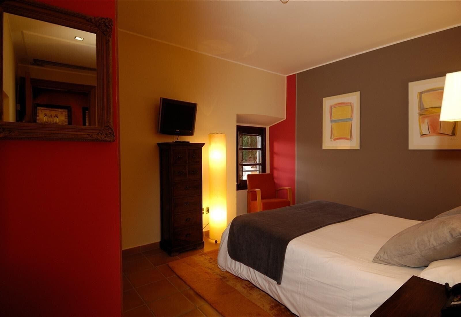 Un cuarto de hotel con una cama, televisión, cómoda y obras de arte en las paredes.