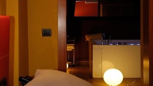 Een hotelkamer met een bed, nachtkastje, lamp, kleine kitchenette met een spoelbak en een raam.