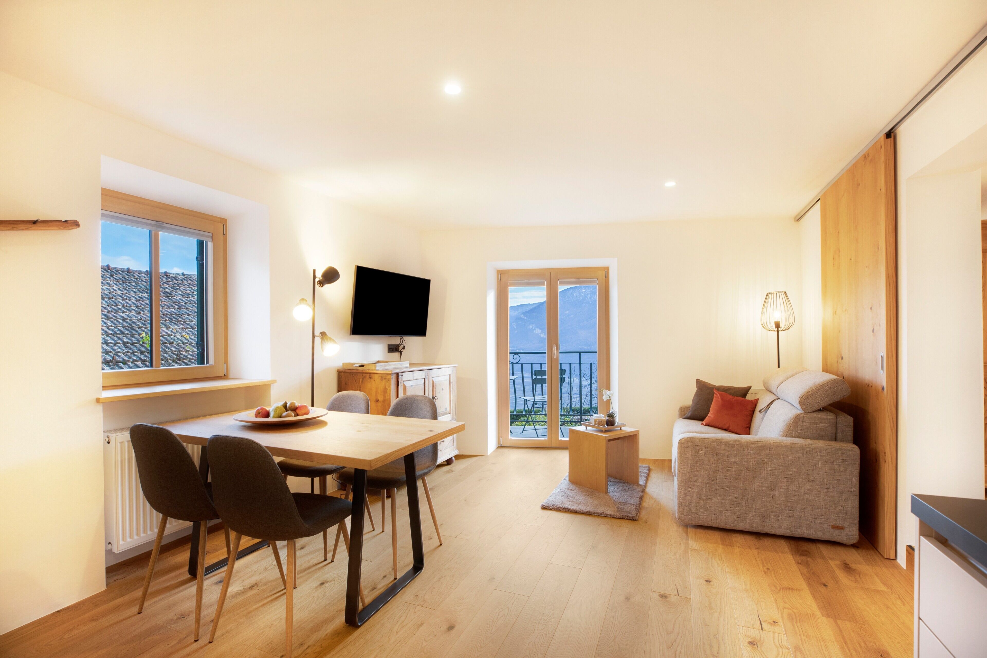 A modern living room with a dining area, a sofa, a TV, and a balcony with a view.