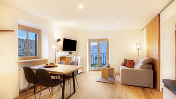 A modern living room with a dining area, a sofa, a TV, and a balcony with a view.