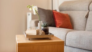 Una mesita de madera con un jarrón de flores blancas, un frasco de vidrio y una pequeña planta en maceta.
