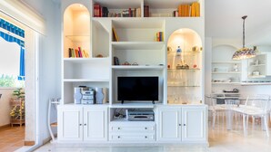 Ein modernes Wohnzimmer mit Flachbildfernseher, weißen Schränken und einem Glastisch.