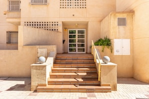 Une entrée d’immeuble avec un escalier menant à une porte, une boîte aux lettres et une petite plante placée sur le côté droit.