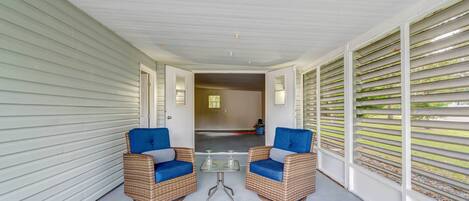 A covered porch with two wicker chairs and a small table, leading to a garage.