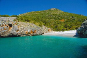 Un paisaje costero con un litoral rocoso, agua turquesa cristalina y una colina con vegetación escasa.