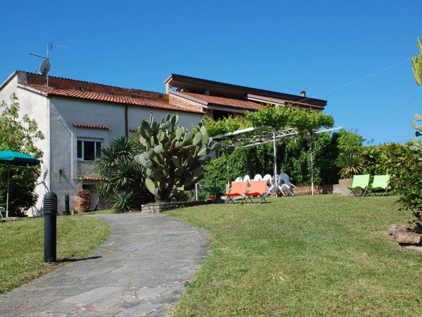 Una casa con un camino empedrado que lleva a un jardín con mobiliario exterior y una gran planta de cactus.
