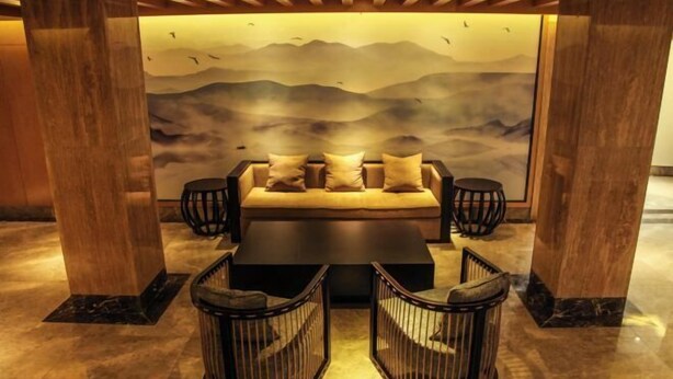A modern lounge area with a sofa set, two side tables, and a wall mural depicting a mountainous landscape. - Guyang Hotel (Guzhen)
