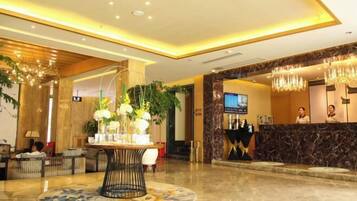 A hotel lobby with a reception desk, a round table with a vase of flowers, and a chandelier.