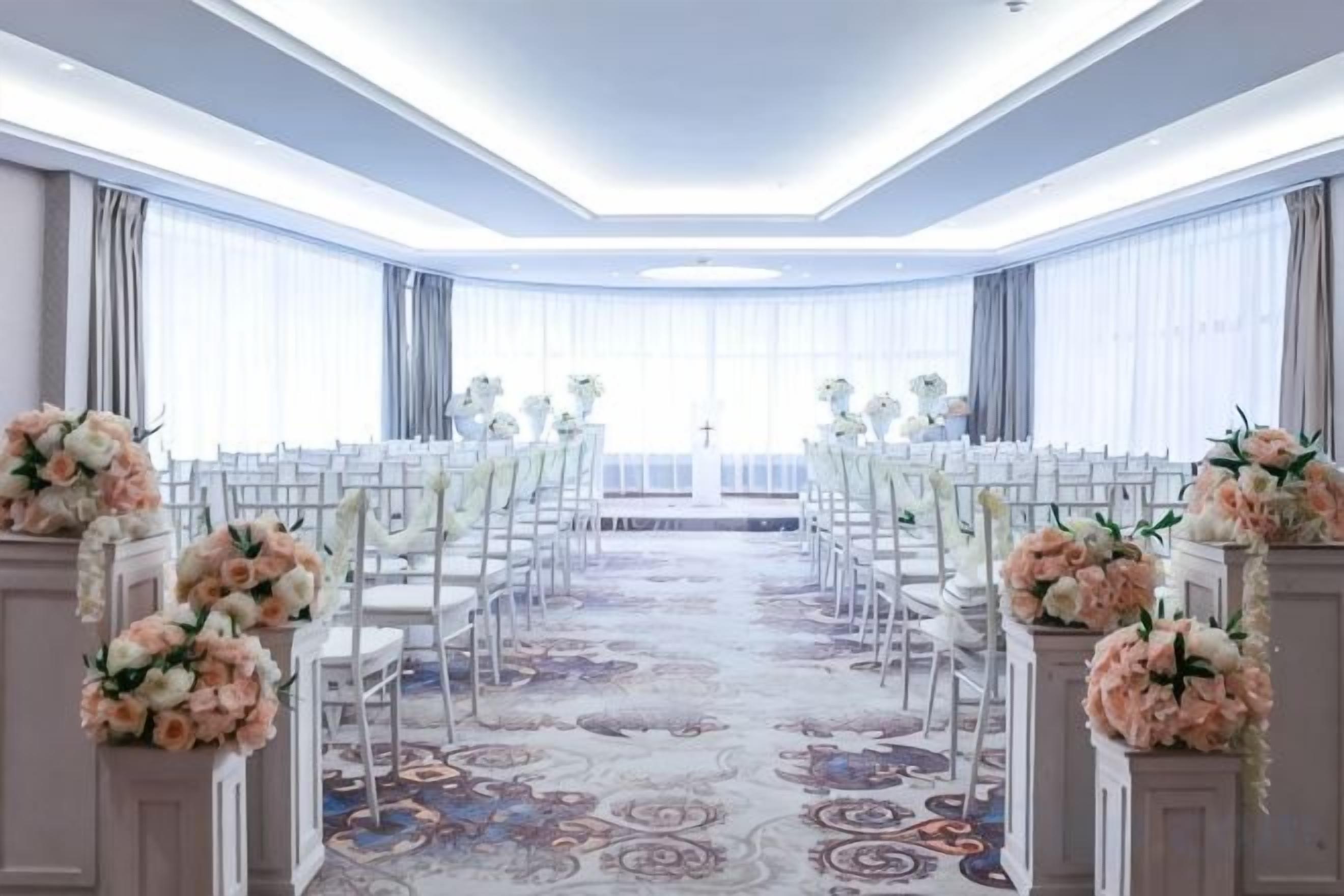 A conference room with rows of white chairs, floral centerpieces, and a patterned carpet.