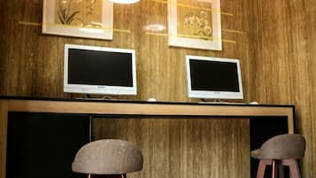 A room with two monitors on a wooden wall, a blackboard below, and two stools.