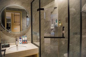 A modern bathroom with a glass-enclosed shower, a round mirror, and a vanity with toiletries. - Guyang Hotel (Guzhen)