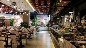A restaurant with multiple dining tables and chairs, a bar area, and a counter with food displays.