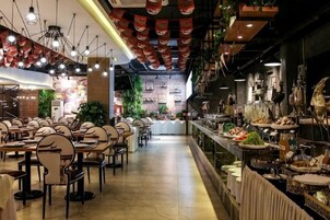 A restaurant with multiple dining tables and chairs, a bar area, and a counter with food displays.