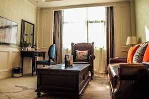 A well-furnished living room with a dark wooden coffee table, a blue armchair, a brown leather sofa, and a large window with curtains. - Guyang Hotel (Guzhen)