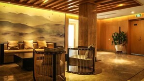 A lobby with a sofa, two circular seating areas, a large pillar, and a wall with a mountain landscape mural. - Guyang Hotel (Guzhen)