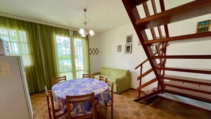 A dining area with a round table, chairs, a green sofa, and a staircase.