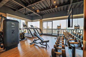 A gym with cardio equipment, weight benches, and a large mirror.