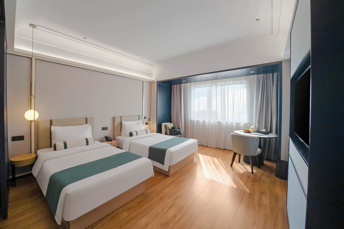 Een hotelkamer met twee bedden, een bureau, een stoel, een televisie en een raam met gordijnen.