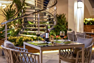 An outdoor dining area with a spiral staircase, wicker chairs, and a table set with wine glasses and plates.