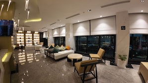 Een moderne hotel lobby met een zithoek, een receptiebalie en een groot raam met uitzicht over de stad.