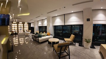 A modern hotel lobby with a seating area, a reception desk, and a large window offering a city view.