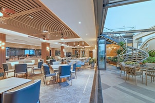 A modern indoor space with a mix of seating areas, including tables and chairs, and a spiral staircase leading to an upper level.
