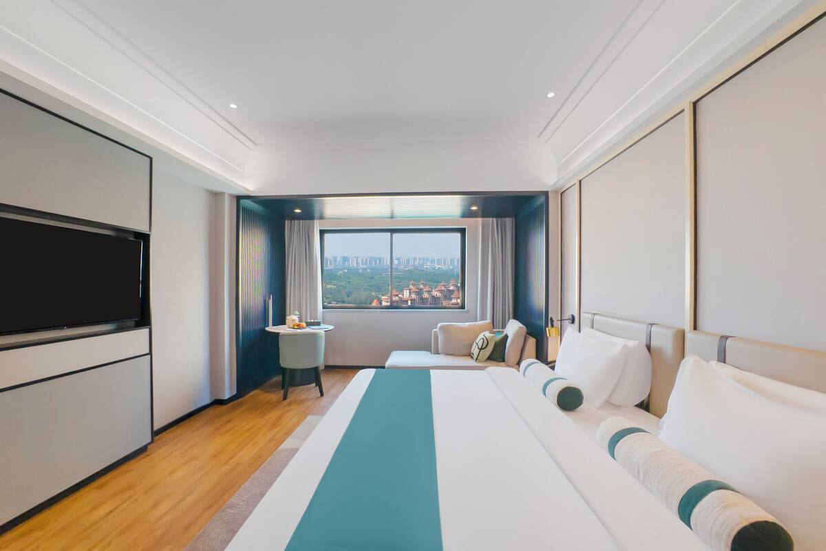 Een hotelkamer met een groot bed, een televisie, een klein tafeltje en een raam met uitzicht op de stad.