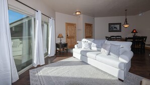 Un salon spacieux avec un canapé blanc, un tapis à motifs et un coin repas comprenant des chaises et une table en bois.